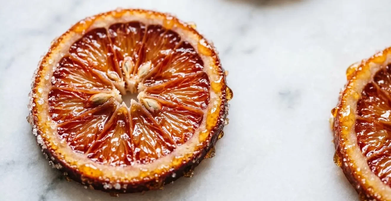 Tranches d'orange confite translucides disposées sur une surface claire avec un sirop brillant