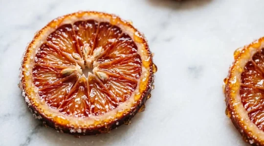 Tranches d'orange confite translucides disposées sur une surface claire avec un sirop brillant