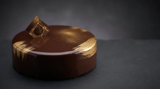 Entremet moderne décoré avec élégance de touches dorées subtiles sur glaçage miroir chocolat noir